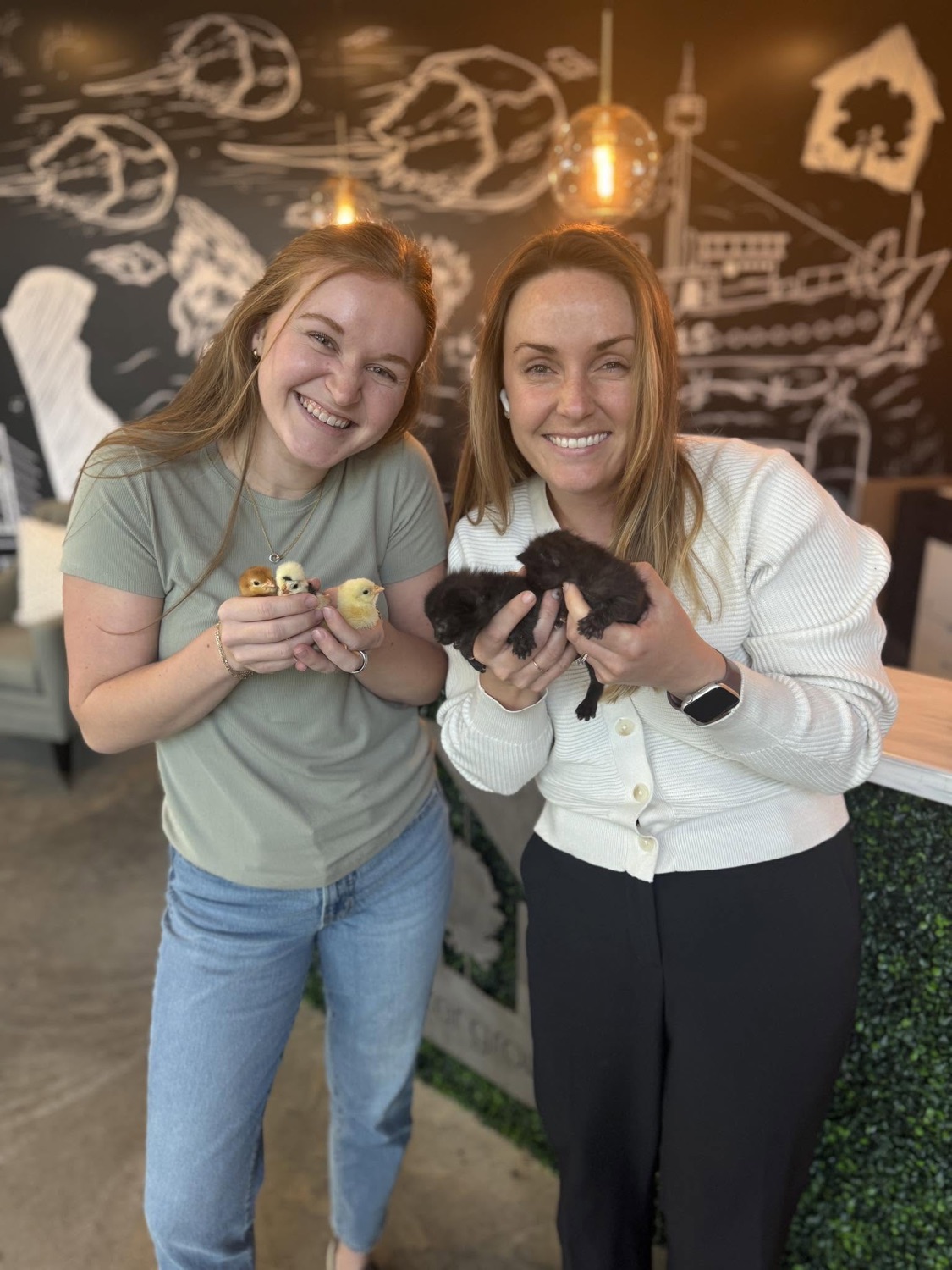 Two team members smiling while holding baby chicks and a kitten